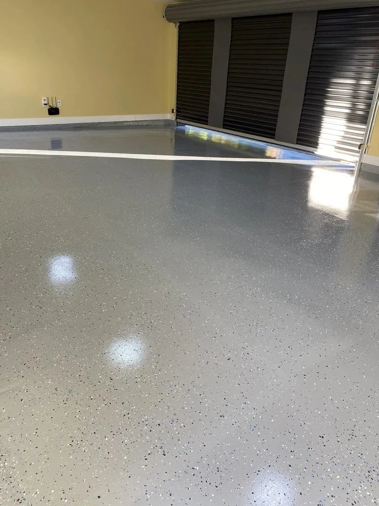A residential garage floor in Burnaby coated in epoxy, with decorative flake broadcast into the surface while it was still wet. The grey ground and the flake together hide dust and tyre marks, and the coating takes the heat, the turning friction and the oil that a garage floor gets.